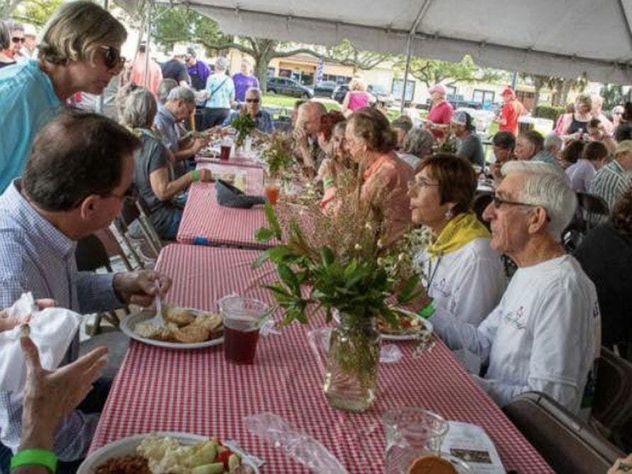 People sitting at at long tables under a tent at the annual Laura Riding Jackson Poetry & BBQ event